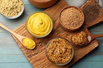 Different types of mustard on light blue wooden table, flat lay