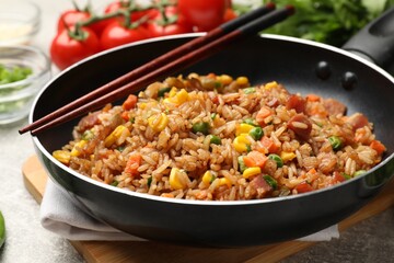 Delicious fried rice in frying pan and chopsticks on grey table, closeup