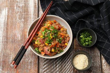 Delicious fried rice in bowl served on wooden table, flat lay