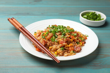 Delicious fried rice with vegetables and bacon served on light blue wooden table, closeup
