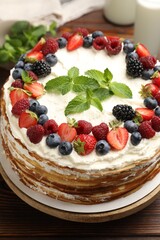 Delicious crepe cake with fresh berries on wooden table, closeup