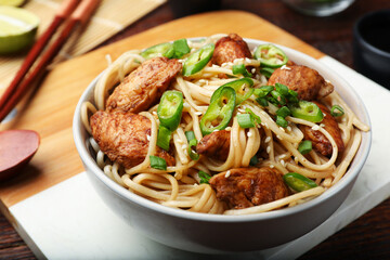 Tasty noodles with chicken, green peppers and sesame seeds served on wooden table, closeup