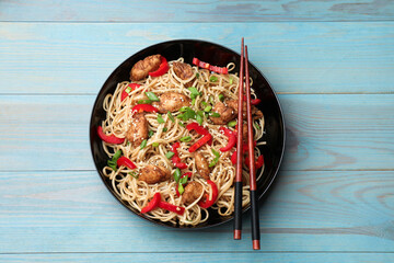 Tasty noodles with chicken, green onions and vegetables served on blue wooden table, top view