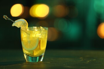 Glass of alcoholic cocktail with lemon slices on table against blurred background. Space for text