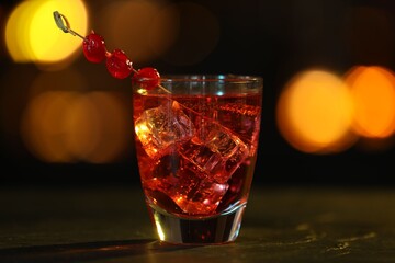 Glass of alcoholic cocktail with cherries on table against blurred background