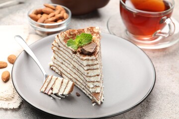 Piece of tasty crepe cake with cocoa powder, chocolate and nuts served on light table, closeup