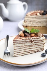 Piece of tasty crepe cake with cocoa powder, chocolate, nuts and blackberry served on light table, closeup