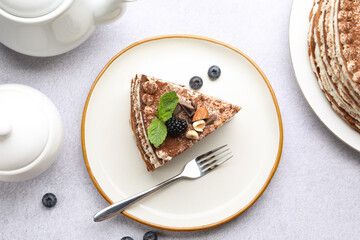 Piece of tasty crepe cake with cocoa powder, chocolate, nuts and blackberry served on light table, flat lay