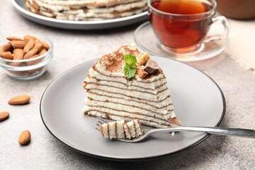 Piece of tasty crepe cake with cocoa powder, chocolate and nuts served on light table, closeup