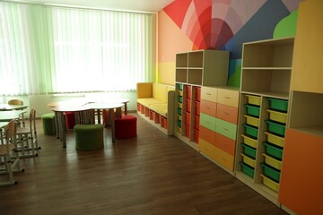 Desks, chairs and shelving unit near bright wall in classroom