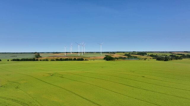Aerial view of wind turbines standing tall amidst the green fields, contrasting with the clear blue sky, Br&uuml;ssow Uckermark, Brandenburg, Germany.