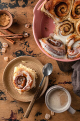 Freshly baked cinnabon bun served on ceramic plate and coffee cup on wooden textured background. Top view