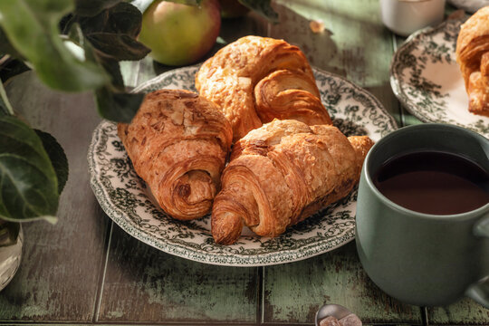 Breakfast on a wooden table with croissants, coffee and apples in bright light of the morning sun. Cozy rustic autumn food concept