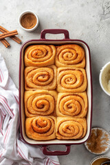 Freshly baked cinnabon buns in a ceramic baking dish on light gray background top view. Making cinnamon rolls process