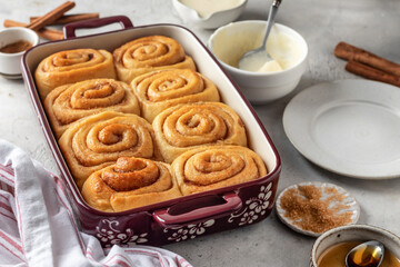 Freshly baked cinnabon buns in a ceramic baking dish on light gray background. Making cinnamon rolls process