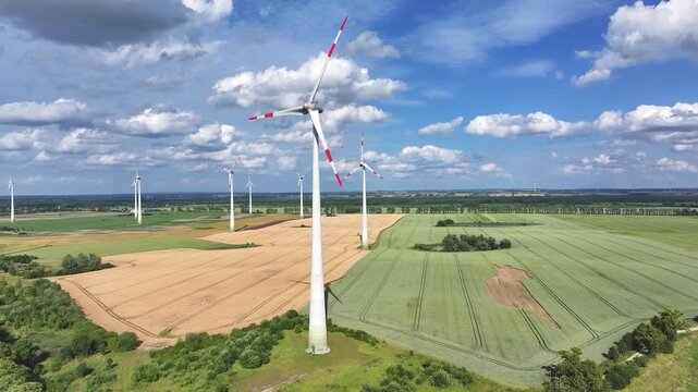 Aerial view of several wind turbines stand tall amid golden and green fields under a partly cloudy sky, creating a striking contrast, Br&uuml;ssow Uckermark, Brandenburg, Germany.