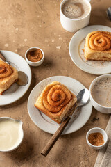 Freshly baked cinnabon roll buns served on ceramic plates with coffee on brown textured background. Cozy autumn menu concept