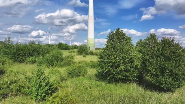 Aerial view of towering wind turbines standing amidst lush green fields and vibrant vegetation under a partly cloudy sky, Br&uuml;ssow Uckermark, Brandenburg, Germany.