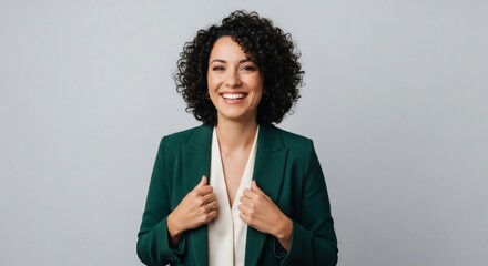 Woman in green blazer and cream blouse smiling broadly against a grey background