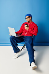 Stylish young man in a beanie and red jacket engages in work with a laptop