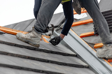 Construction worker carefully places roof tiles on a sloped surface while standing on top of a building  showcasing the effort involved in roofing work