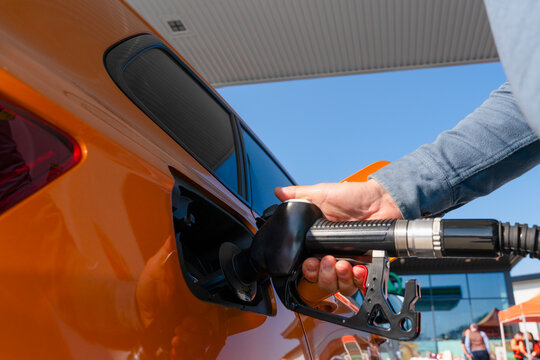 Close-up of a Man refuelling orange car at gas fuel station. Male filling diesel at petrol station using a fuel nozzle