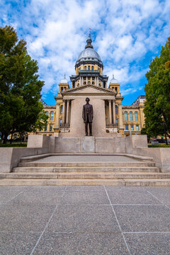Front entrance of the French Renaissance and Italianate style Illinois state capitol building with zinc alloy coated dome in downtown Springfield with Lincoln statue in the foreground.