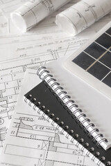 sustainable architecture tools and materials: blueprints, solar panel, wood textures, fabric swatches, and stones. Eco-friendly design, conscious construction and green innovation.