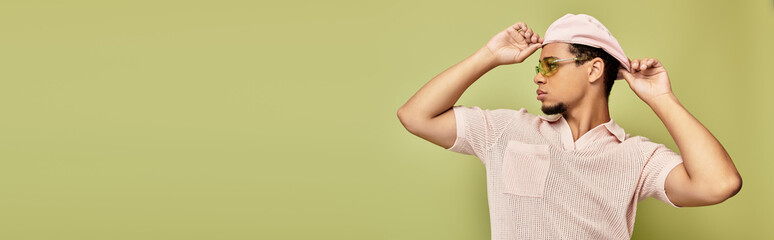 Stylish young man in pink polo and flat cap poses confidently against green backdrop