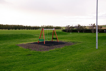 Fototapeta premium Playground swing set in Akranes surrounded by vibrant green grassy fields