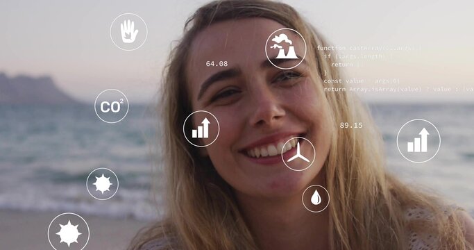 Smiling blonde woman standing on beach with digital overlays showing CO2 icon, other icons and code