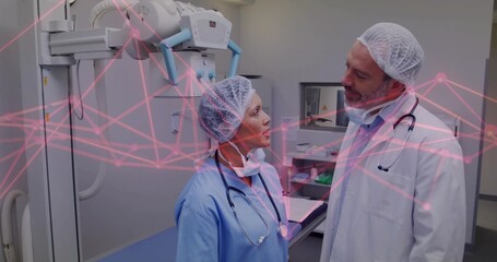 Doctor and nurse analyzing X-ray scan under ceiling-mounted tube in radiology, wearing stethoscopes
