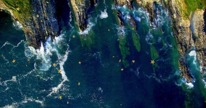 Fototapeta Crashing waves sending white sea foam over jagged rocks along coastline, with golden star graphics