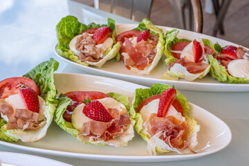 Fresh bite-sized salad cups with lettuce, prosciutto, strawberries, and creamy cheese, perfect for casual gatherings and healthy snacking, ideal for sharing at parties
