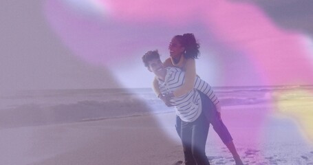 Giving piggyback ride couple in casual wear at shoreline with lapping ocean waves, pastel flares