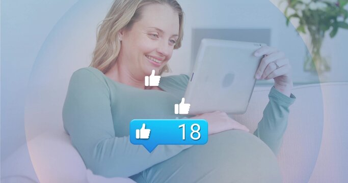 Reclining pregnant woman holding tablet on sofa in living room, floating icons, notification bubble