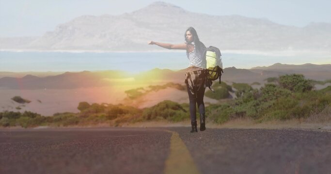 Hitchhiking female traveler extending thumb on paved coastal road, with backpack and plaid shirt - Powered by Adobe