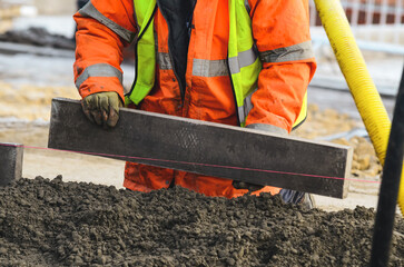 Close-up of construction worker leveling concrete and placing edging pin kerb on construction site