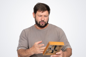 Bearded man holding vintage wooden abacus, looking confused and puzzled. Funny concept of outdated accounting, retro business tool, meme idea of dumb accountant not understanding.
