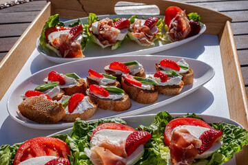 Fresh bite-sized snacks on a wooden tray featuring lettuce, strawberries, and prosciutto, perfect for casual gatherings and sharing at parties with friends and family