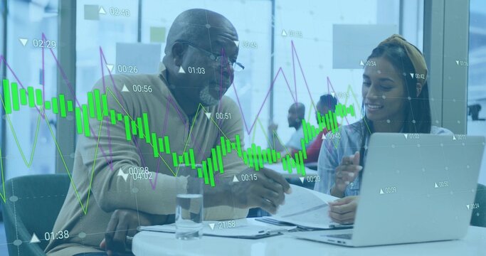 Senior consultant and mentee reviewing printed documents and laptop at office, with stock charts - Powered by Adobe