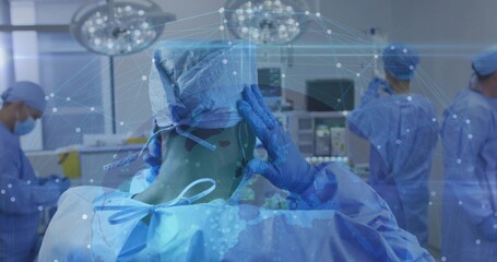 Positioning surgeon adjusting cap in operating room, with overhead lights and vital monitors