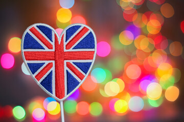 Heart-shaped Union Jack embroidery with colorful bokeh lights in the background, symbolizing...