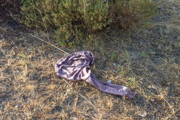Abandoned clothes polluting the environment near green bush