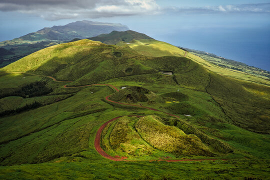 Two volcanic hills of Pico da Esperan&ccedil;a on S&atilde;o Jorge Island, Azores, Portugal, connected by a gentle red sandy path winding through lush green terrain under a clear blue sky
