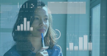 Analyzing woman wearing denim shirt holding pen to lips at office, with charts, graphs, gauges