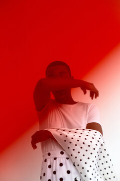 Young Black woman standing with arm raised covering part of face, wearing polka dot garment, posing against red and background, looking away from camera, fashion concept