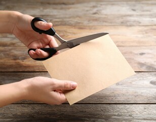 Hands using black scissors to cut blank brown paper envelope on rustic wooden table surface