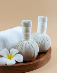 Close-up of herbal compress ball on wooden tray with orchid flower and white towel, luxury spa therapy