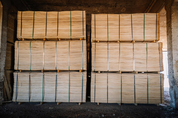 Stacks of processed wood veneer sheets neatly bound with straps and stored on pallets in an industrial warehouse setting.